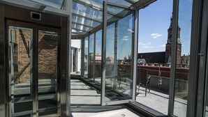 Ein moderner, gläserner Balkon mit Blick auf ein historisches Gebäude und einen Kirchturm.