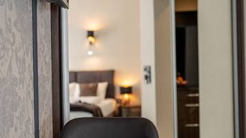 A breakfast table with croissants, orange juice, and a plate, in a hotel room with a bed and a nightstand in the background.