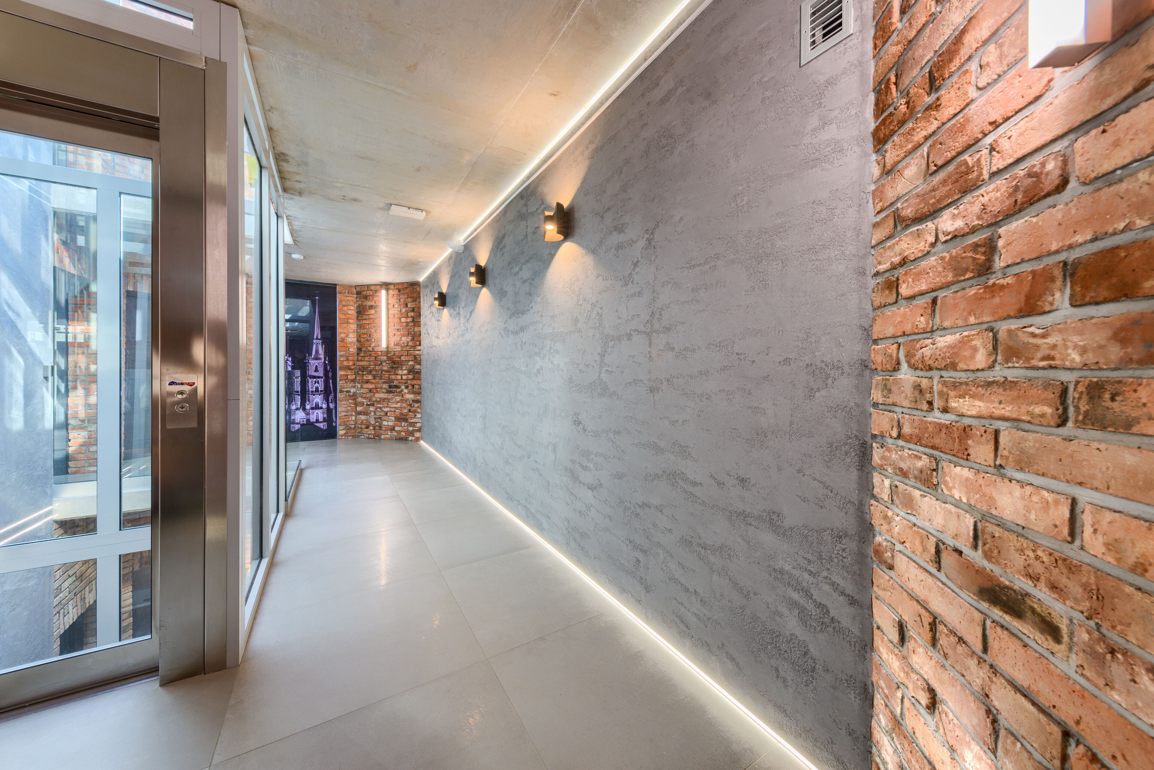 A modern hallway with a glass door, a brick wall, and a light strip along the floor.