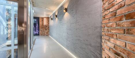 A modern hallway with a glass door, a brick wall, and a light strip along the floor.