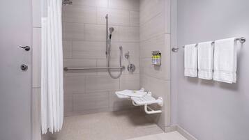 Une salle de bain moderne dotée d’une douche à l’italienne, de barres d’appui, de toilettes avec un siège de sécurité et d’un porte-serviettes muni de plusieurs serviettes.