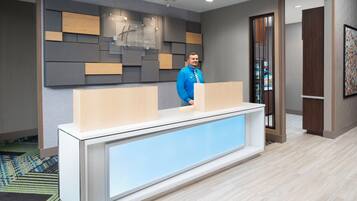 A reception desk with a modern design, a man standing behind it, and a patterned carpet.