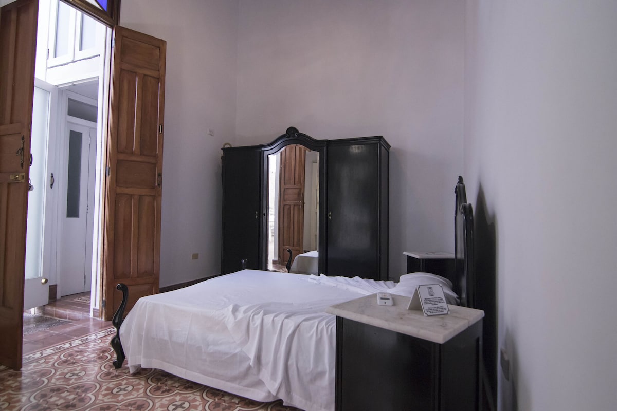 Ein Schlafzimmer mit Bett, Kommode, Spiegel und einer Tür zu einem anderen Raum.