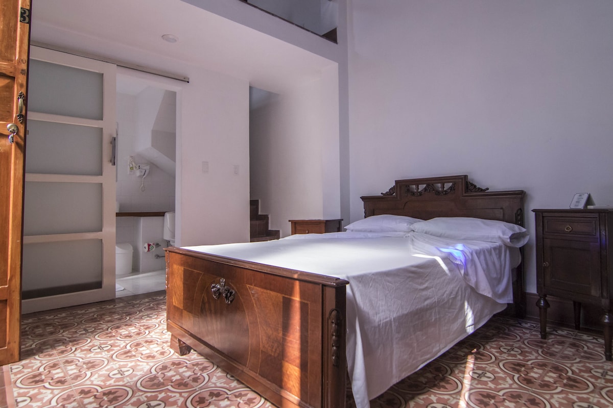 Ein Schlafzimmer mit einem hölzernen Bett, einem Nachttisch, einer Kommode und einem Badezimmer mit Badewanne und Toilette.