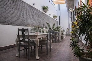 Un pasillo estrecho con pared de ladrillo, piso de baldosas y un comedor con mesa y sillas.