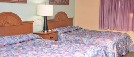 A hotel room with two beds, a nightstand, a lamp, and two framed pictures on the wall.
