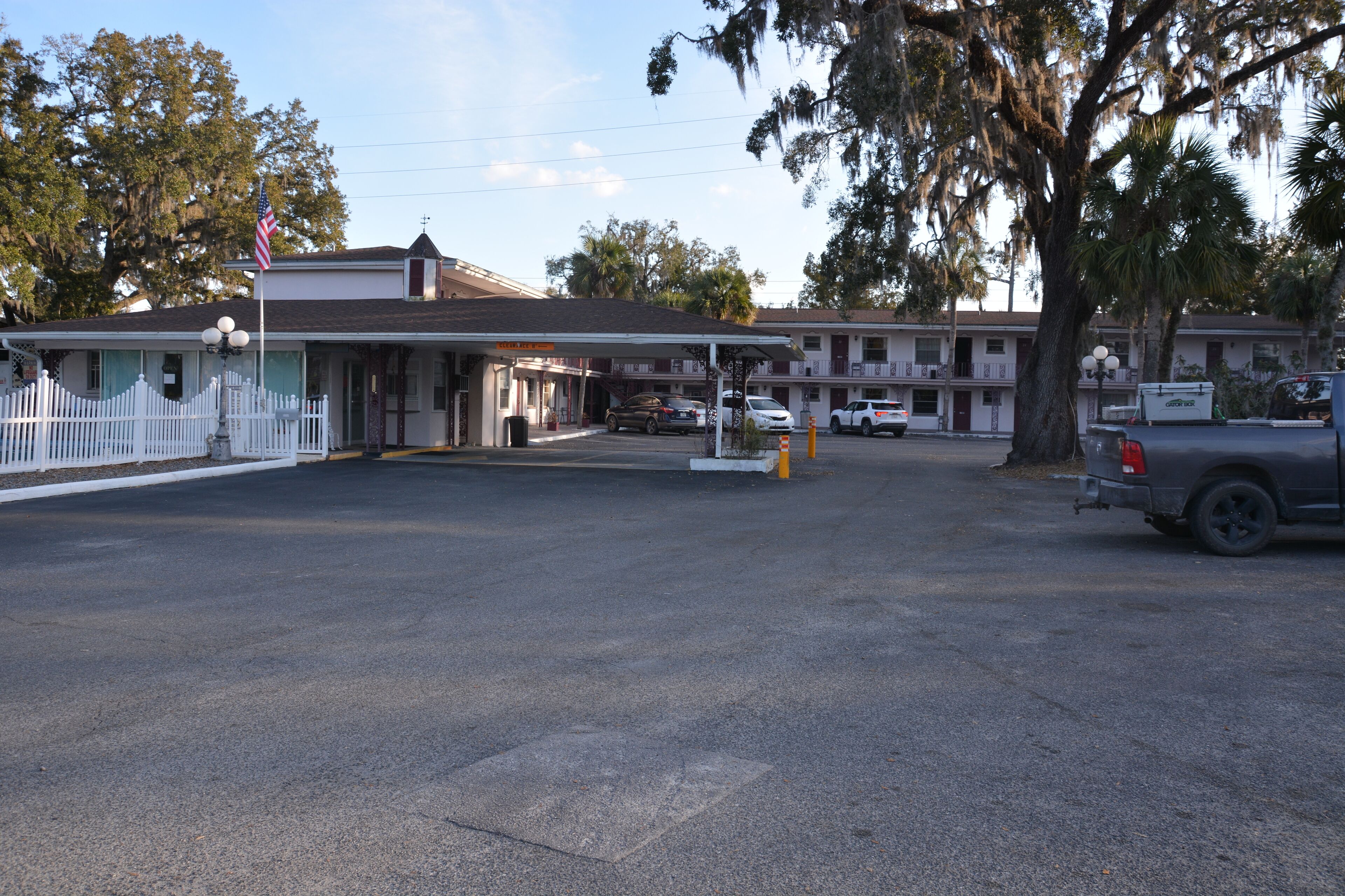 Een motel met een witte hek, een benzinestation en een parkeerplaats.