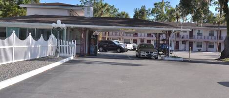 A motel with a white picket fence, a covered parking area, and a sign indicating 'Clearance 8'.