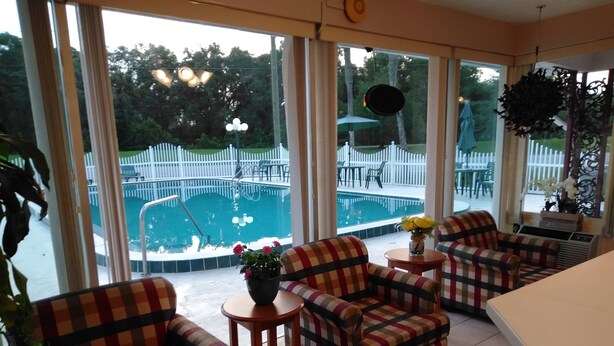 Ein Zimmer mit großen Fenstern, Blick auf einen Pool, karierten Sofas und einem kleinen Tisch mit Blumen.