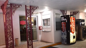 Ein Hotel Eingang mit aufwendigen roten Säulen, einer Coca-Cola-Getränkeautomaten und einer Glastür, die nach innen führt.