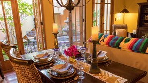 Una mesa de comedor dispuesta con platos, vasos y velas, rodeada de sillas de mimbre.