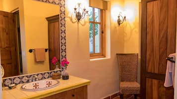 Un baño con un espejo grande, un lavamanos con azulejos decorativos, una ventana y una silla.
