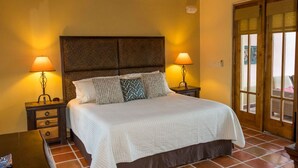 Una habitación de hotel con una cama grande, dos mesitas de noche con lámparas, un cabecero de madera y un ventanal corredero que da a un espacio exterior.