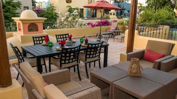 Un patio exterior con zona de comedor, mobiliario de mimbre y un elemento decorativo en la pared.