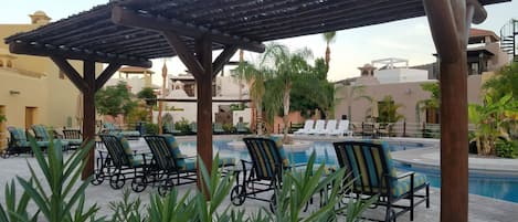 Un área junto a la piscina con sillones de descanso y una pérgola.