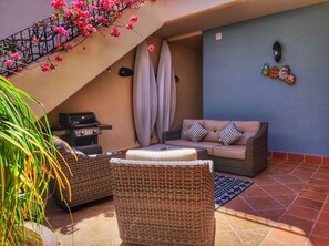 A patio with wicker furniture, a grill, and a blue wall.