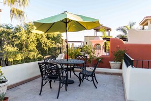 Eine Terrasse im Freien mit Tisch und Stühlen, einem grünen Sonnenschirm und Topfpflanzen.