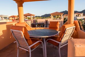A terrace with a round table and two chairs, surrounded by orange cushions.
