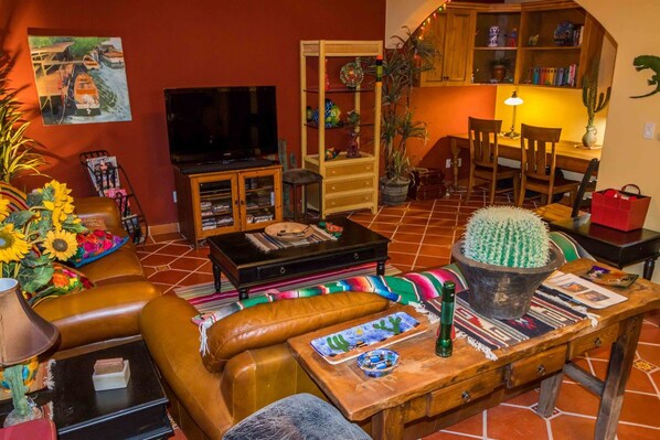 Una sala de estar acogedora con televisor, sofá de cuero, mesa de centro de madera y un cactus como elemento decorativo.