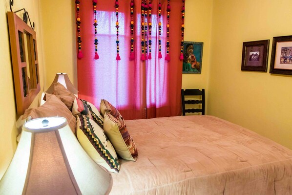 A bedroom with a bed, pillows, a lamp, a chair, and a window with curtains.