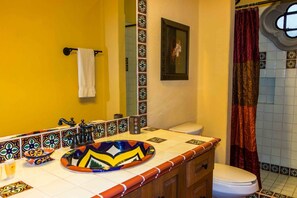 A bathroom with a yellow wall, a white toilet, a sink with a colorful basin, and a shower curtain.