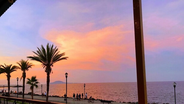 A sunset view from a balcony overlooking a beach with palm trees and a promenade. - Casa Corazon FN 164 2 BR by Casago (Loreto)