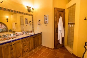 Un baño con tocador de madera, un espejo grande y zona de ducha con azulejos.