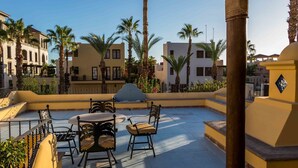 A rooftop terrace with outdoor seating, palm trees, and buildings in the background. - Casa Colette FN 307 2 BR by Casago (Loreto)