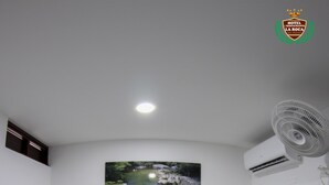 A hotel room with a bed, a nightstand, a wall-mounted fan, an air conditioning unit, and a painting of a landscape.
