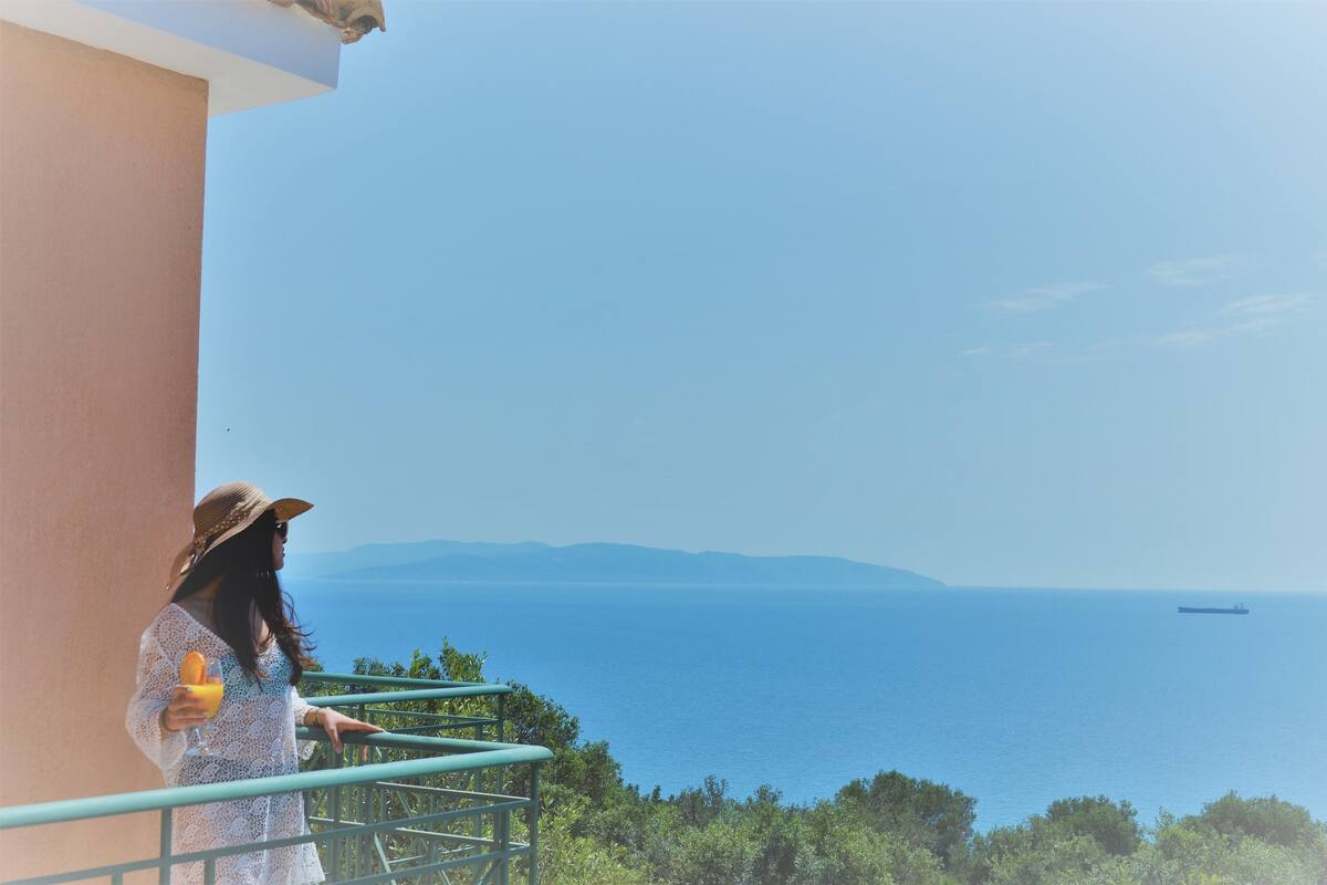 A balcony with a view of the sea and distant mountains.