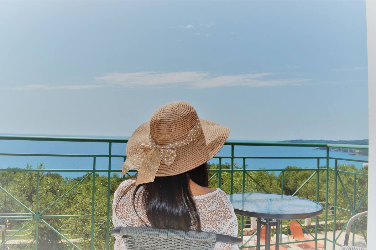 A person seated at a table with a view of a body of water and greenery.