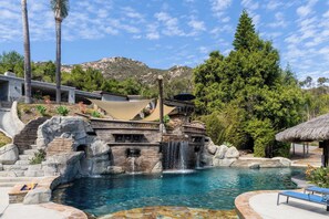 A pool with a waterfall, surrounded by rock formations and palm trees. - Luxury Private Resort | Pirate Ship Pool & Theater (Escondido)