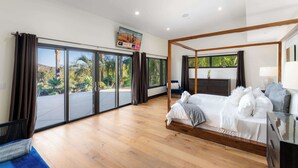 Une chambre moderne avec un lit à baldaquin, de grandes portes-fenêtres coulissantes et un téléviseur à écran plat fixé au mur.