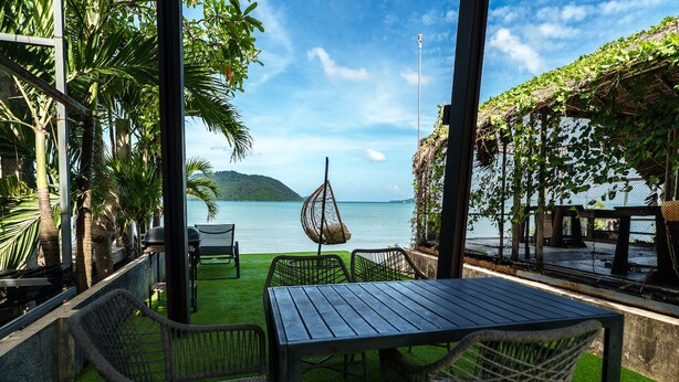 A covered outdoor seating area with a view of the sea, featuring a table and chairs, and a hanging chair. - Chocolate Beachfront 2 BR Pool Villa (Tambon Rawai)