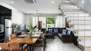 A modern living room with a wooden dining table, black sofas, and a staircase. - Chocolate Beachfront 2 BR Pool Villa (Tambon Rawai)