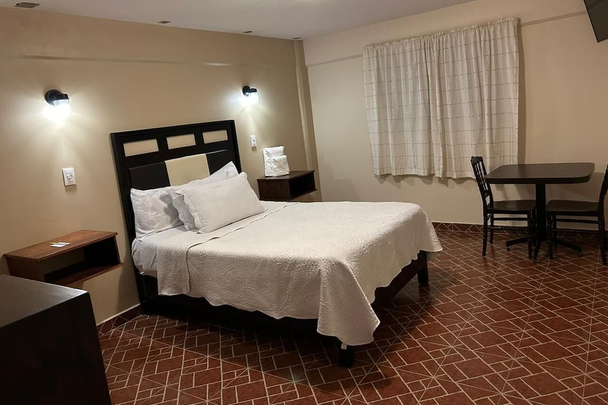 Un dormitorio con una cama, mesitas de noche, una pequeña mesa y un rincón de comedor con sillas.