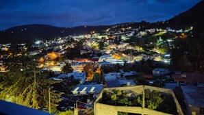 Vista nocturna de un pueblo en la ladera de una colina, con numerosos edificios y farolas.