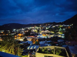 Vista nocturna de un pueblo en la ladera de una colina, con numerosos edificios y farolas.