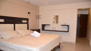 A neatly made bed with a headboard, a bedside table, a mirror, and a shelf with toiletries.