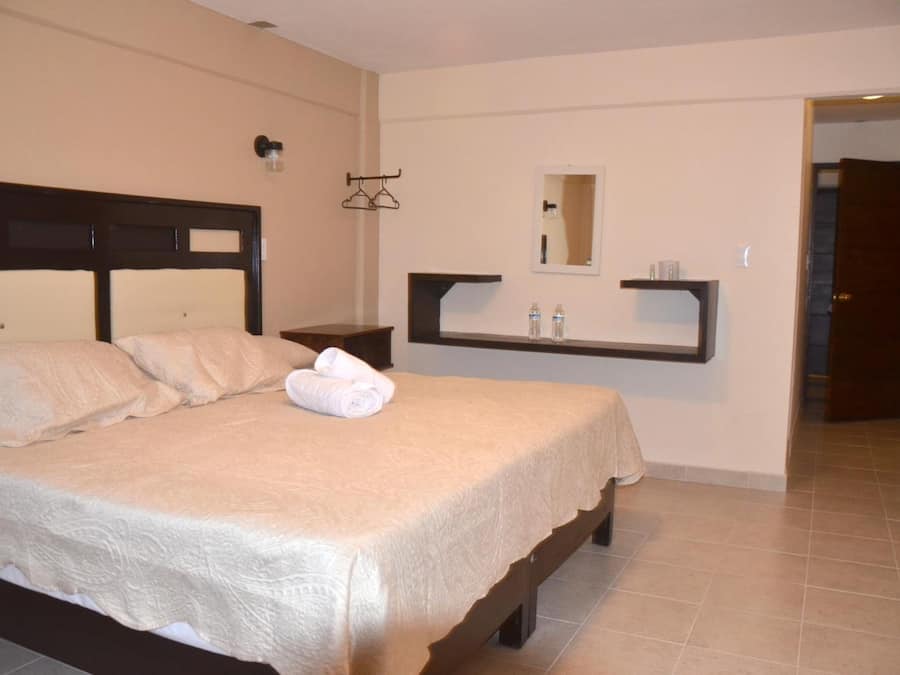 A neatly made bed with a headboard, a bedside table, a mirror, and a shelf with toiletries.