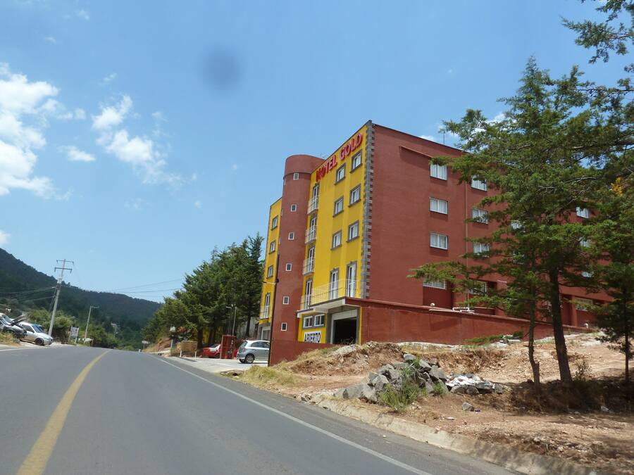 Um hotel com vários andares, fachada amarela e vermelha, entrada visível e uma estrada em primeiro plano.