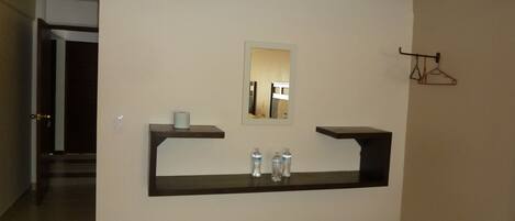 A hallway with a dark counter, a mirror, and a hanging clothes rack.
