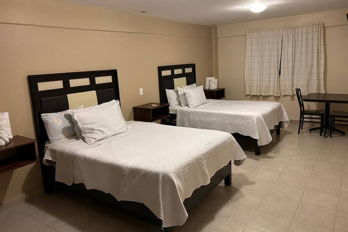 Habitación de hotel con dos camas, una mesa de comedor y una ventana con cortinas.