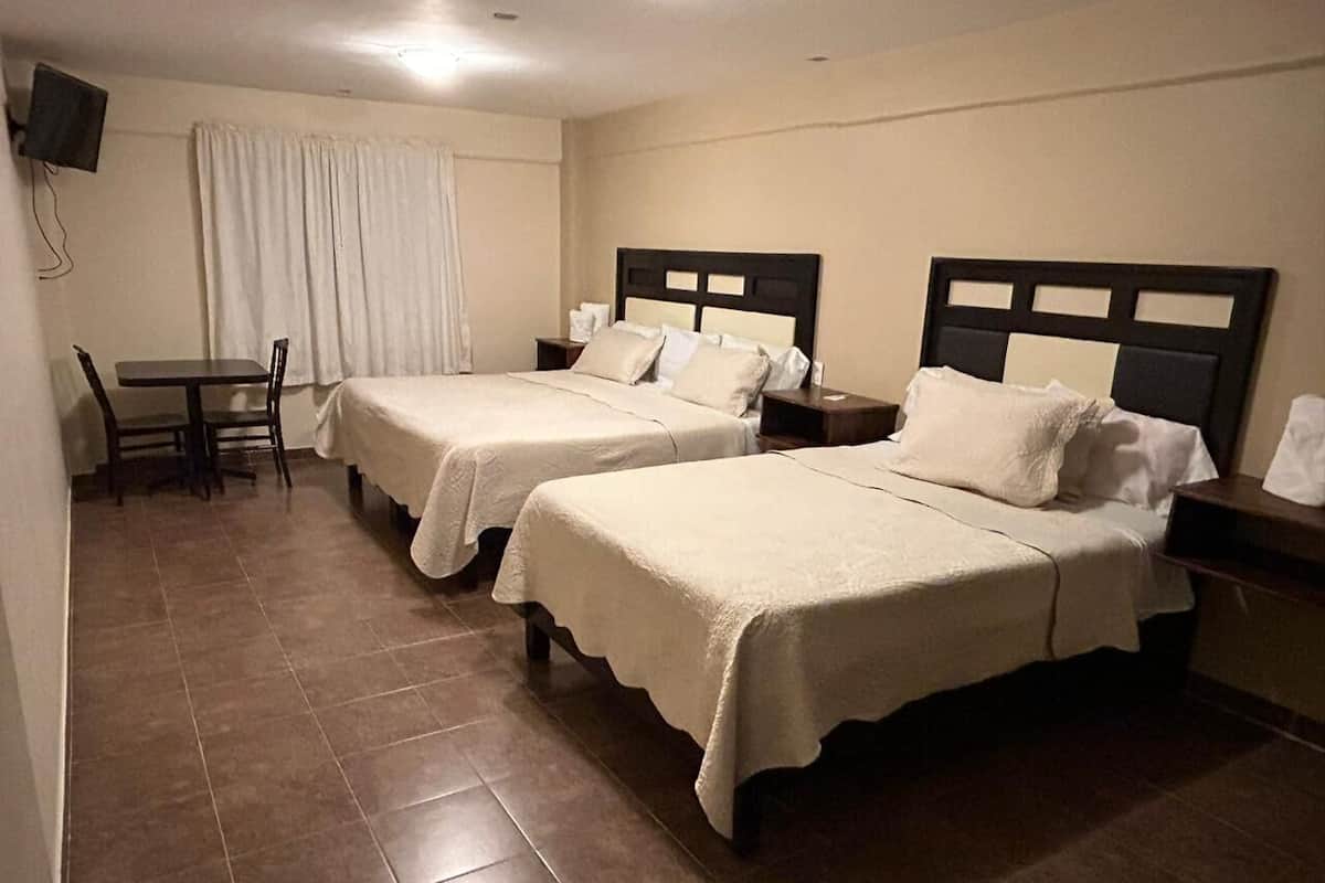 Habitación de hotel con dos camas, una mesita y un televisor.