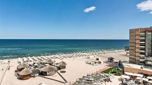 A beach resort with a large building, numerous sun loungers, and thatched-roof structures.
