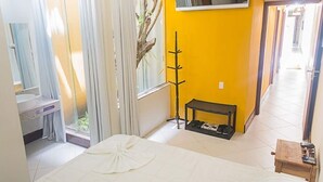Ein Schlafzimmer mit Bett, einer Bank, einem Kleiderständer und einem Fenster mit Vorhängen.