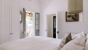 Une chambre à coucher avec un grand lit, des murs blancs et une porte donnant sur un balcon.
