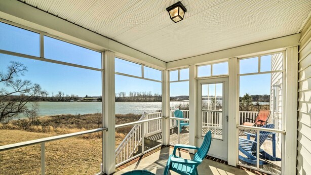 Een overdekt terras met uitzicht op een meer, met blauwe Adirondack-stoelen en een witte balustrade.
