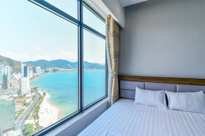 Habitación de hotel con un ventanal grande que ofrece vistas a una ciudad costera y montañas.