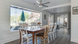 A dining area with a wooden table and chairs, large windows, and a ceiling fan. - Private Beach • Hot Tub • Sauna • Game Room •  No-Wake Cove + Party Cove Access (Coloma)